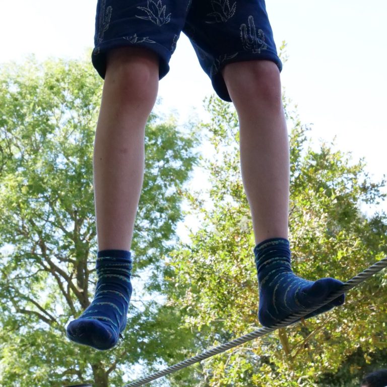 Tight wire legs Legs facing camera of a white boy wearing blue shorts and socks. One foot balances on a tight wire, the other foot is in mid air.